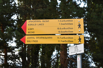 Tourist sign in Mestia, Svaneti, Georgia. Giving directions on the trail leading to Koruldi Lakes. Information sign with distance, estimated time of the route. Text in English and Georgian