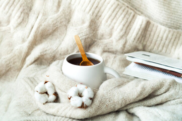 White cup tea on knitted texture with dried cotton. Cozy breakfast in Scandinavian. Christmas greeting card. Creative copy space.