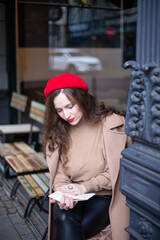 Pretty woman with curly hair in red french beret reading the book in the street