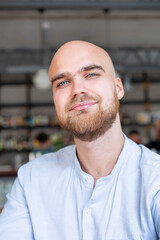 Obraz premium Portrait of smiling white european bald man with beard and grey eyes in light blue shirt in the workspace