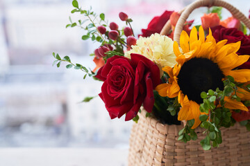 Close-up of a basket with beautiful autumn flowers made of red roses, sunflowers and green leaves. The concept of the holiday. Copy space. High quality photo