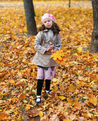 Portrait of a unhappy child in an autumn park. Sad girl standing with fallen yellow leaves.
