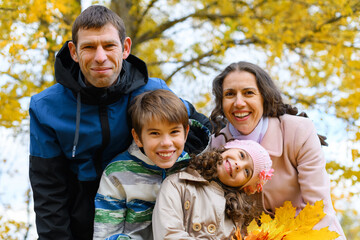 Portrait of a happy family in an autumn park. People pose against the background of beautiful yellow trees. They hug and are happy together.