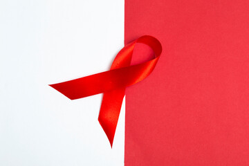 Medical concept for World AIDS Day in December. Red AIDS awareness ribbon on white and red background. Close up