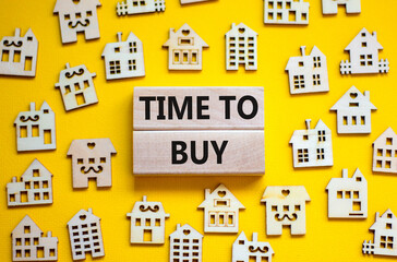 Time to buy house symbol. Concept words 'Time to buy' on wooden blocks near miniature houses. Beautiful yellow background, copy space. Business and time to buy house concept.