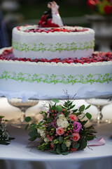 Obraz na płótnie Canvas Traditional white wedding raspberry cake with bouquet on white table. Wedding delicious fruit cake dessert