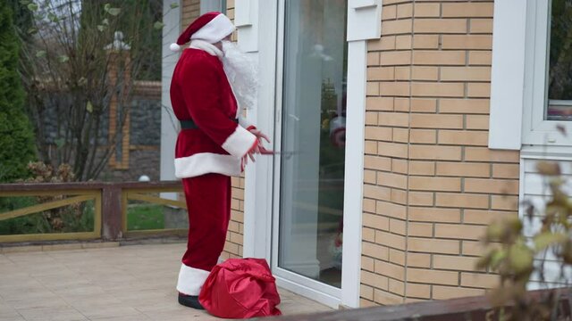 Wide shot thief in Santa Clause costume opening door on backyard on New Year's eve. Young Caucasian male burglar robbing house on Christmas. Robber breaker looking around unlocking door