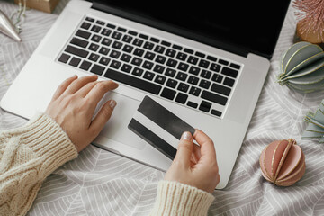 Hands with credit card on laptop with black screen on background of stylish bed with modern christmas ornaments. Christmas sale and shopping online. Space for text. Cyber monday