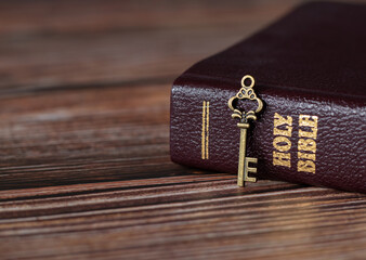A rustic old vintage retro key with closed Holy Bible book with gold text on a wooden table. A...