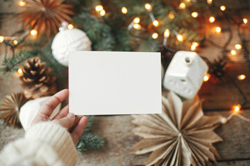 Christmas card mock up. Hand holding empty greeting card on background of christmas stars, baubles,...