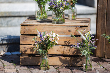 Fototapeta na wymiar Many colourful fresh spring flower bouquets in glass jars stand on wooden box in sunlight