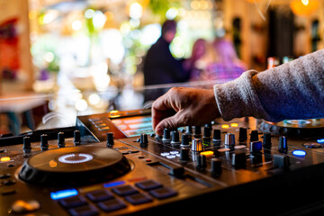 dj hand manipulating the controls of a mixing console in nightclub