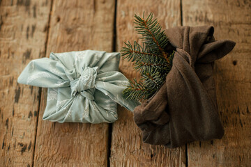 Furoshiki eco friendly presents. Stylish gifts wrapped in fabric with fir branch on rustic wooden table. Zero waste winter holidays and gift. Happy holidays and Merry Christmas