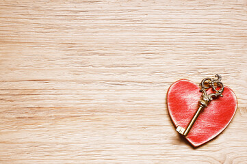 Red heart on the wooden background and key.