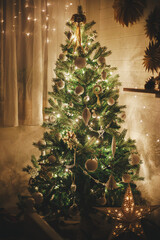 Stylish Christmas tree decorated with modern white baubles, boho ornaments and golden lights. Merry Christmas! Atmospheric festive scandinavian room. Christmas eve. Magic time. Space for text