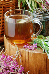 Willow herb fermented herbal tea in glass cup with fresh flowers close on wooden rustic background, traditional russian hot drink, closeup, naturopathy and natural medicine concept