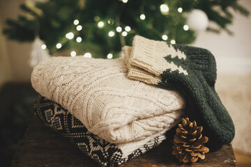 Cozy knitted sweaters and wool socks on rustic wood with pine cone on background of christmas tree...