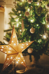 Christmas star on background of christmas tree in lights in evening room. Big paper star garland...
