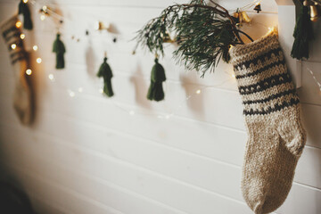 Christmas rustic stocking with fir branch and stylish garland with bells on white wooden wall with...