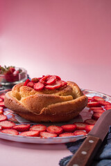 Strawberries, knife and cake with some strawberries on a pink background