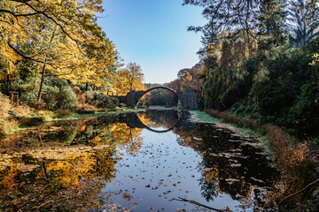 Unique looking bridge Rakotzbrucke,also called Devils Bridge,Saxony,Germany.Built to create circle when it is reflected in waters.Colorful fall landscape.Fantastic autumn foliage.Amazing place