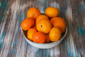 Juicy tangerines in a gray ceramic bowl on a wooden background.