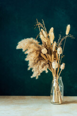 Bouquet of beige dried flowers in a glass vase on green blue background. Home decoration concept.