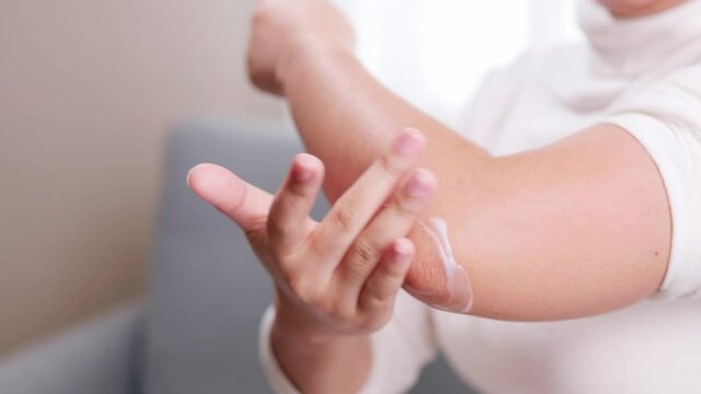 Detail of woman giving pain reliever cream on her elbow due to pain during arm movement.