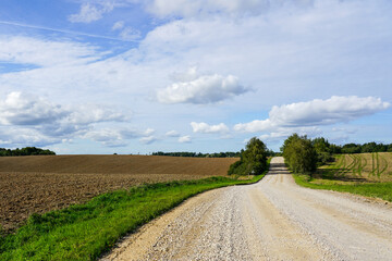 Fototapeta na wymiar beautiful rural landscape with plowed field, gravel road, forest and blue sky