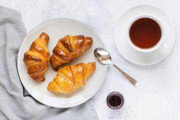 Croissants on light gray plate, small jar of jam and cup of tea. Food background. Breakfast concept.