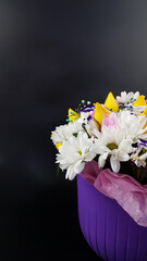 a colorful bouquet of multicolored yellow white and lilac flowers. composition of daisies roses chrysanthemums and carnations on a dark background