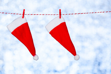 Two red Christmas hats hang from a rope against a blurred shiny blue-gray background. Copy space. Concept