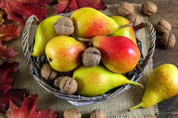 Koszyk z gruszkami i orzechami otoczony kolorowymi liśćmi. Jesienne tło © Monika