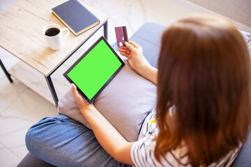 Woman shopping on tablet computer using credit card sitting in sofa. Online shopping
