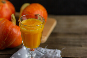 Pumpkin smoothie, spicy latte in a glass. In the background in blur orange pumpkins on a wooden vintage background. Copy space. Cozy table in hygge style