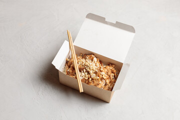 Delivery of Chinese dishes. Chicken with kung pao rice in a paper lunch box. Close-up on a light background