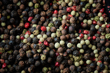 Peppercorns on dark background. Mixed peppercorns background. Different colored peppercorns, close up.