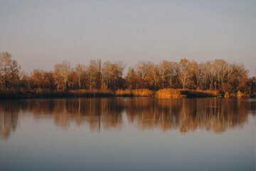 Vivid autumn sunset. Autumn landscape of sunset over river with shining grass on shore. Scenic nature at bright evening with colorful sky