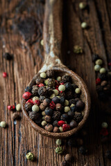 Peppercorns in ceramic spoon over dark wooden background. Mixed peppercorns background. Different colored peppercorns, close up.