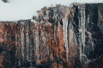 Full frame view of icicles hanging in from an orange rock