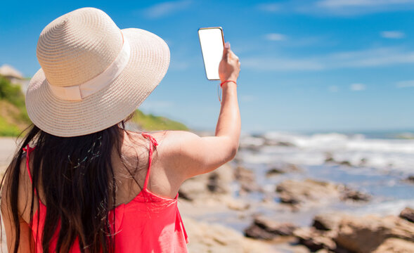 hat woman taking photos at sea, latin girl taking vacation photos, rear view of girl taking selfie on the beach