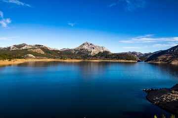 sunrise over beautiful and huge blue lake with blue sky and big limestone mountains. Porma reservoir. Leon Mountains