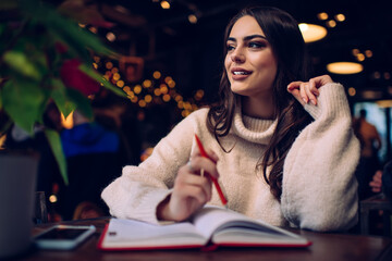 Thoughtful woman writing in planner at cafe