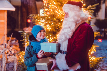 Boy receives a present from Santa Claus himself in front of Christmas tree