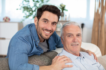 smiling grown son sit on couch relax with senior dad