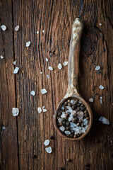 Salt and pepper on an ceramic spoon over wooden backround
