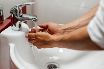 Washing men's hands under running water in the bathroom over the sink.