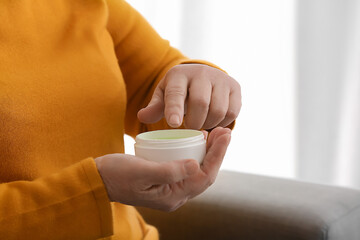 Elderly woman with jar of cosmetic cream at home, closeup