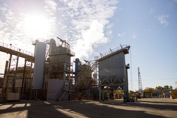 Obraz premium Manufacturing plant with industrial buildings, equipment and ladders under sky with clouds and sun