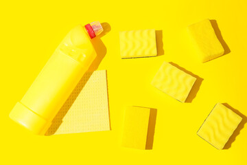 Yellow cleaning sponges and bottle of detergent on color background